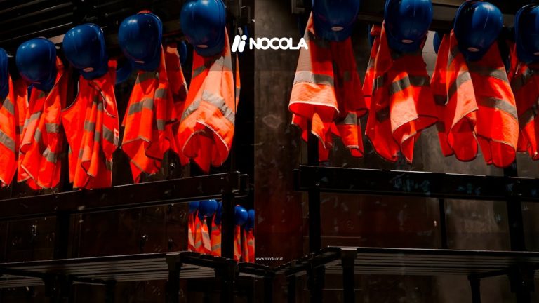 Row of orange safety vests and blue helmets hanging in industrial setting