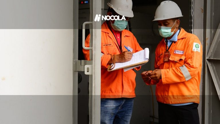 Two construction workers in safety gear discussing plans at a site entrance.