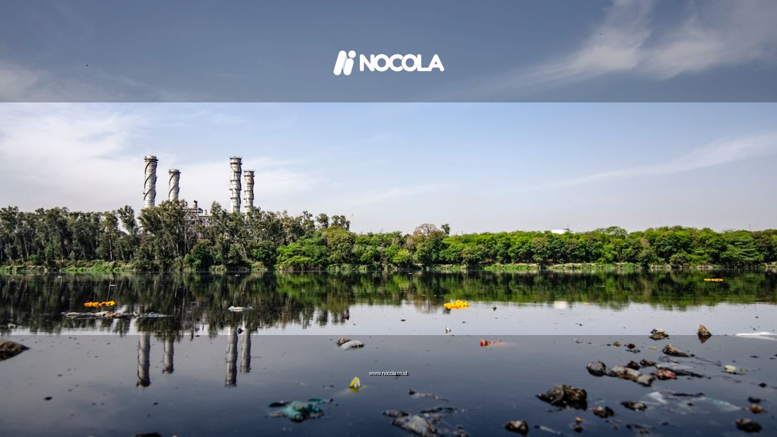 View of a polluted river reflecting factory emissions under a clear sky in India.