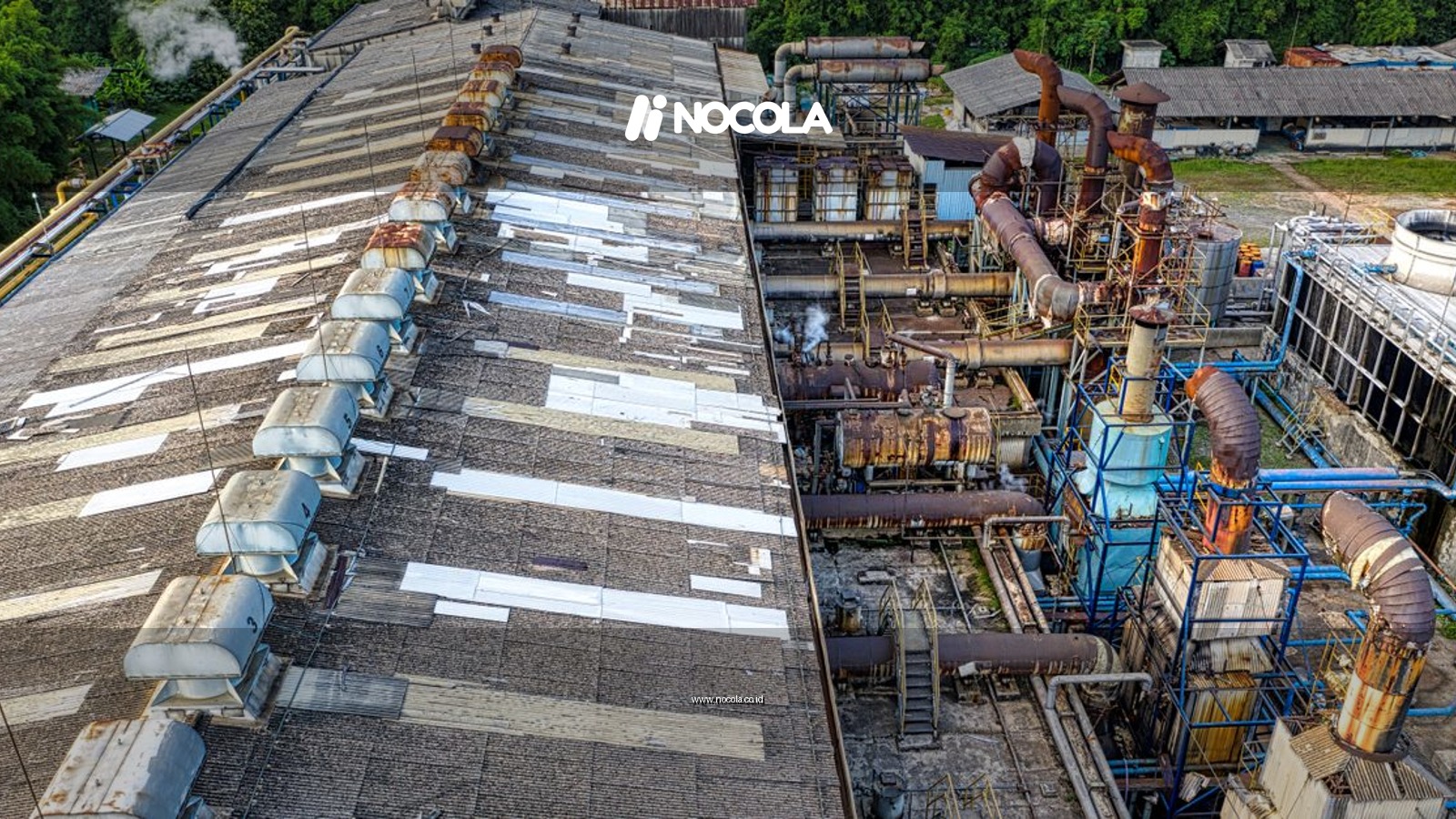 From above of industrial area of factory with large equipment placed in city among green trees in daylight