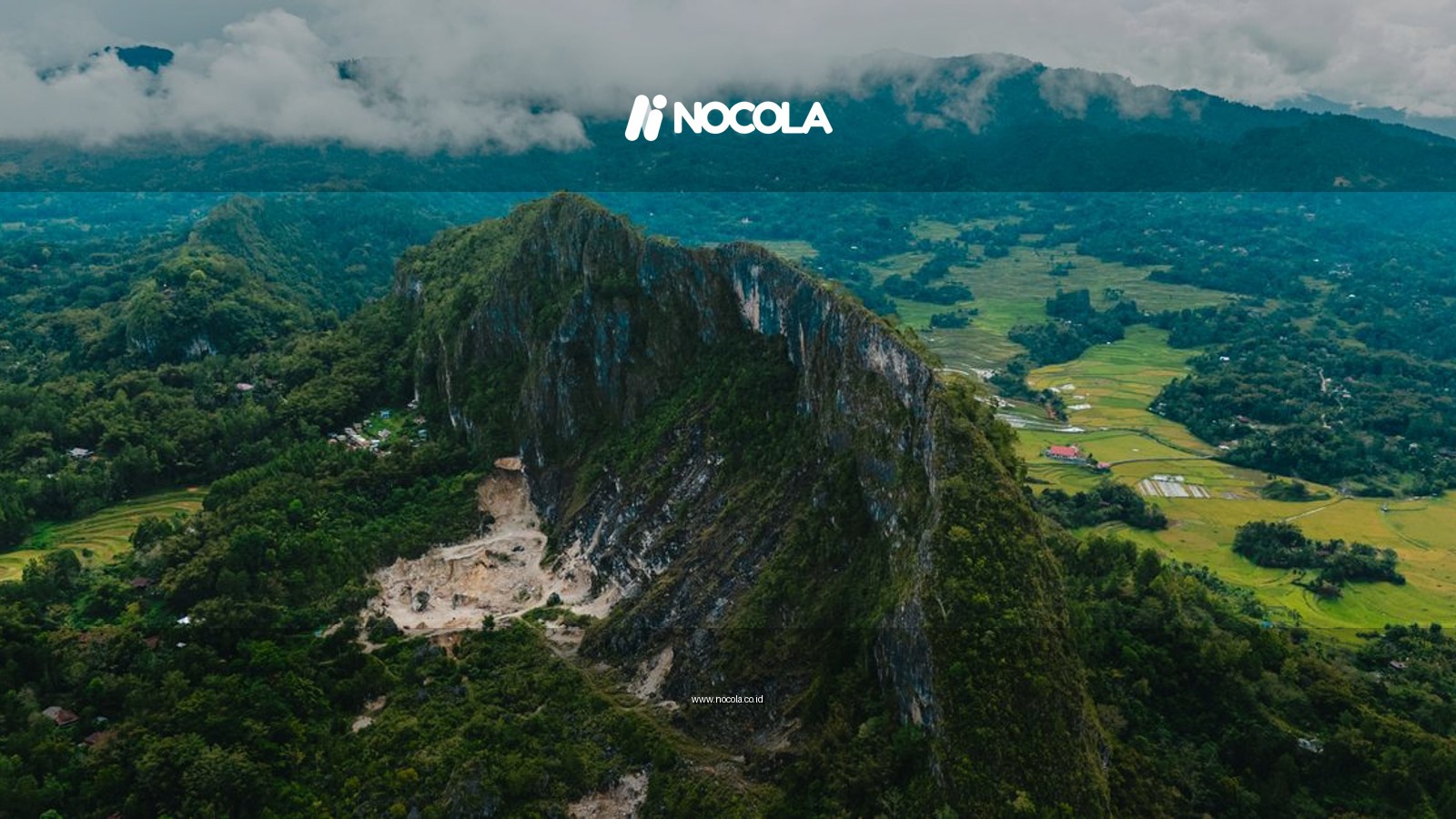 Aerial view of a lush, mountainous landscape in Indonesia with clouds hugging the peaks.
